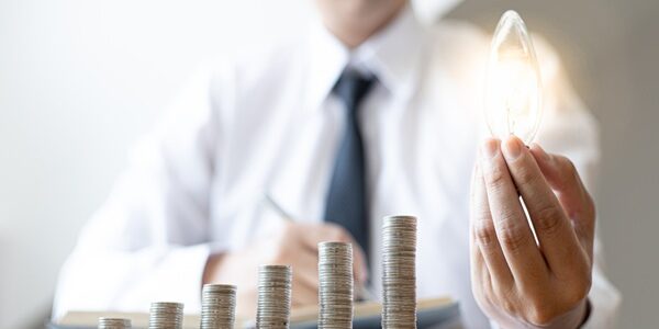 Young,Businessman,Holding,A,Light,Bulb,And,Coins,Or,Money