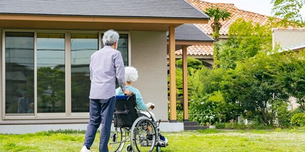 Senior,Couple,In,Wheelchairs,Walking,In,Front,Of,Their,House